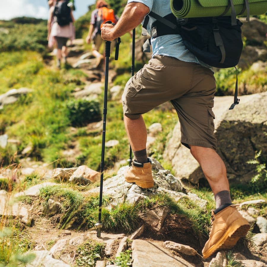 A hiker ascends a rocky trail using trekking poles.