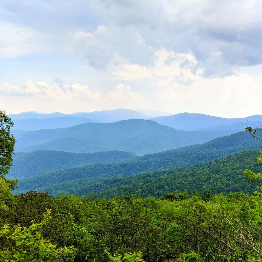 A panoramic view of layered green mountains under a cloudy sky.