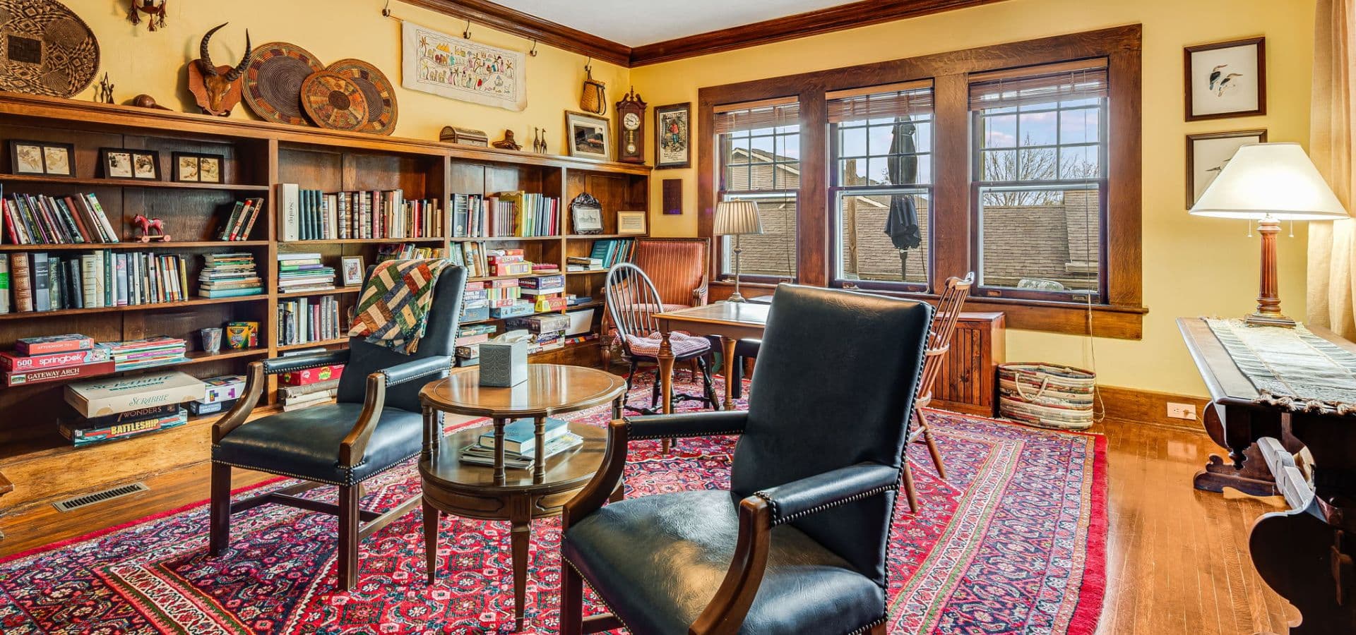 Cozy reading room with wooden bookshelves, two chairs, a coffee table, and large windows.
